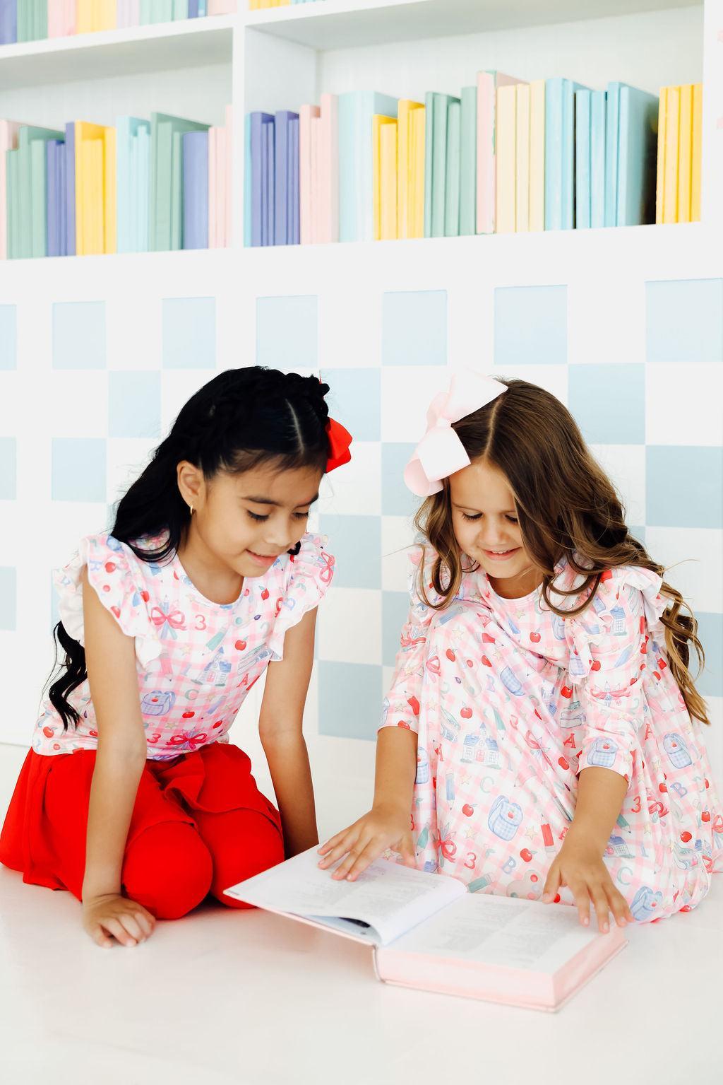a couple of girls sitting on the floor reading a book