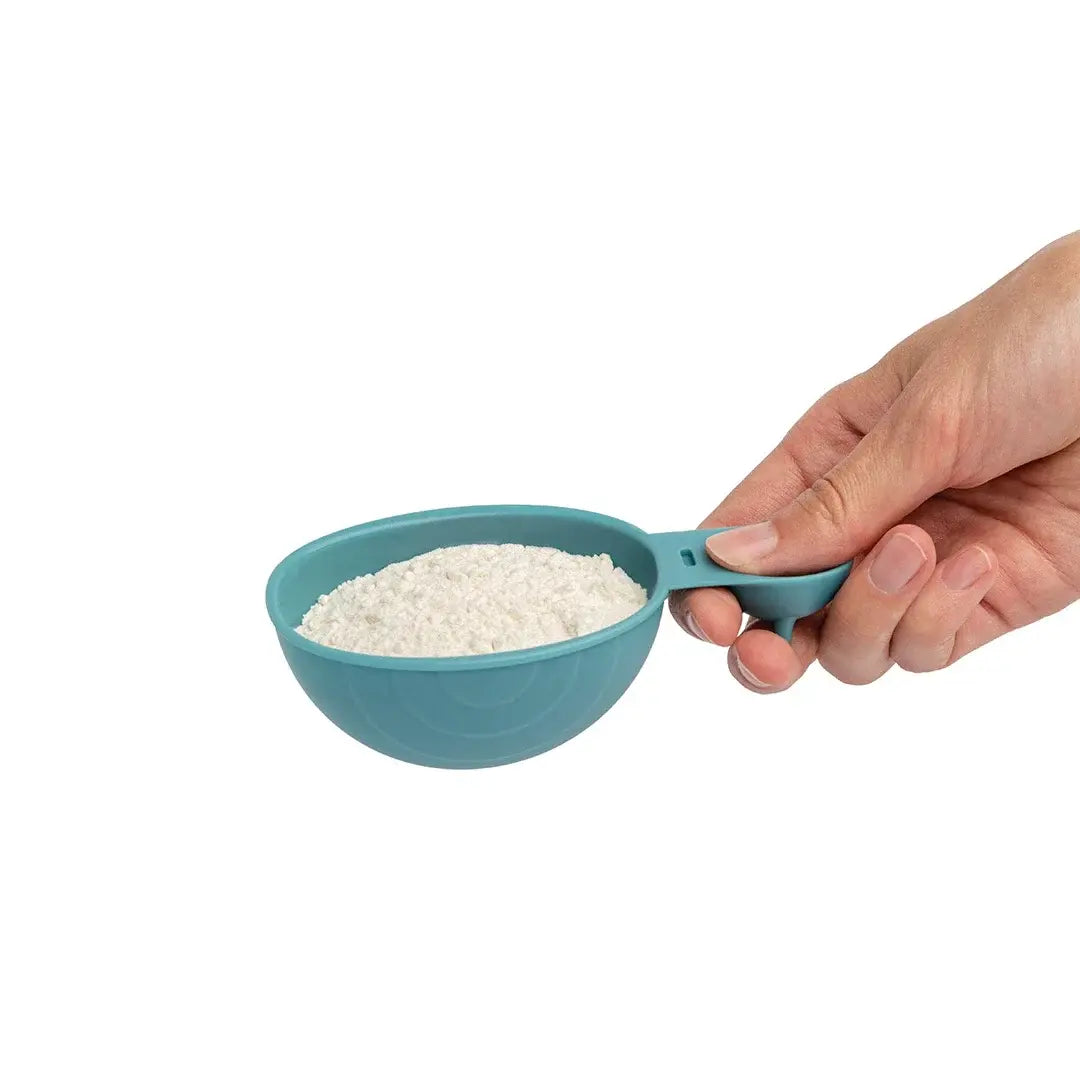 a hand holding a measuring cup with a white powder