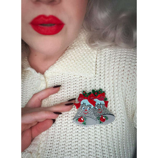 a woman wearing a white sweater with a silver bell pin