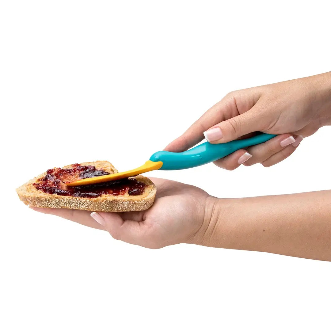 a person holding a piece of bread with jam and a blue utensil