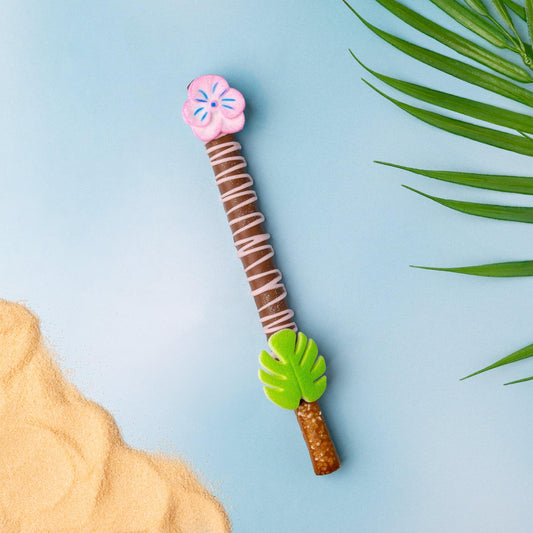 a chocolate stick with a flower on it next to sand and palm leaves