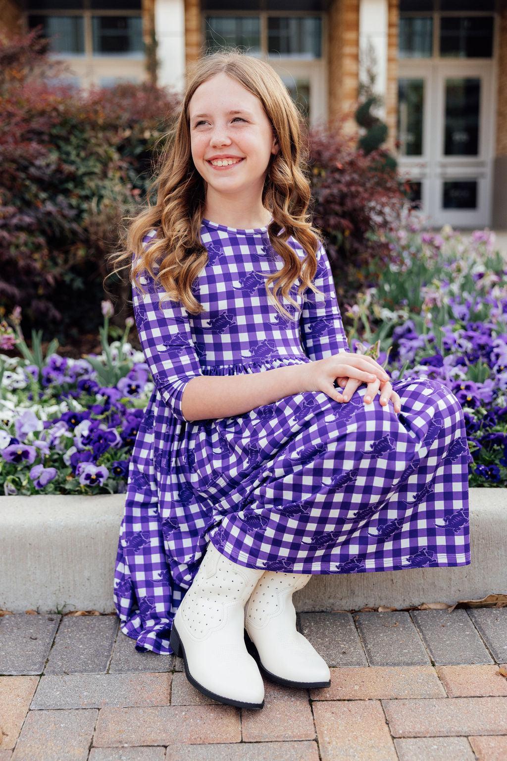 a girl in a purple and white checkered dress sitting on a curb