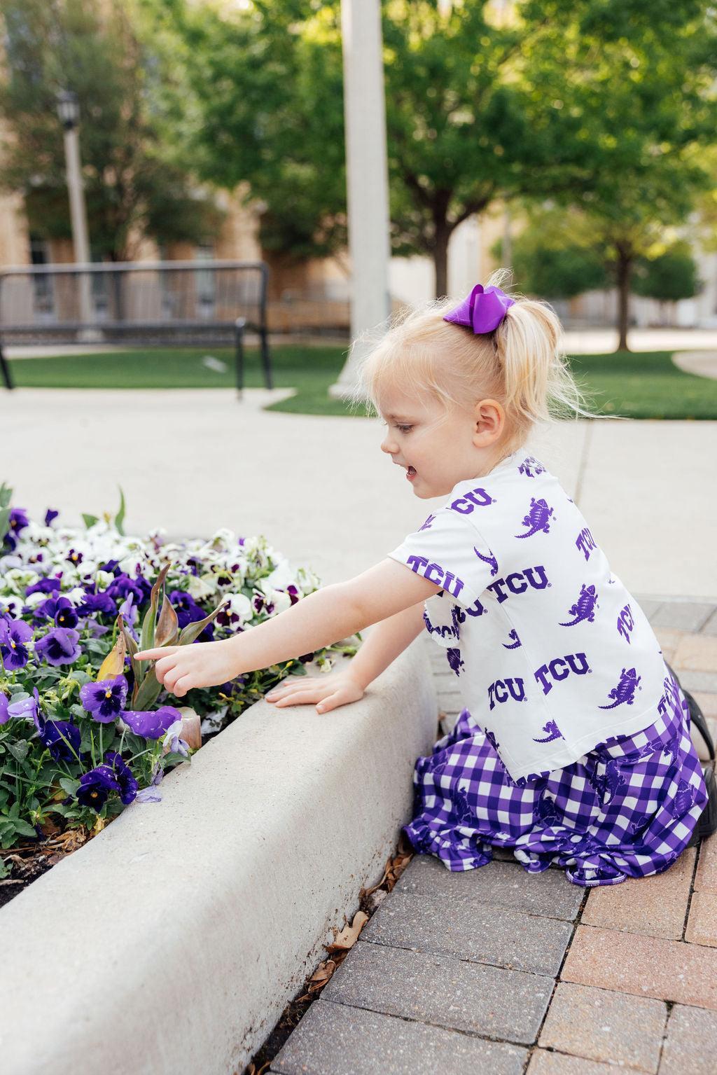 a girl sitting on a curb pointing at flowers