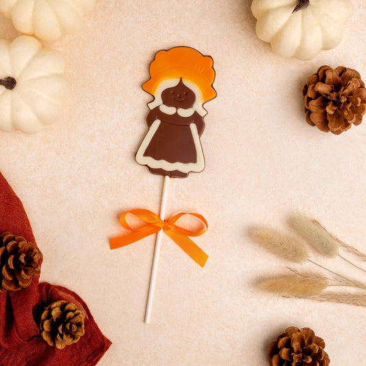 a chocolate candy on a stick next to white pumpkins and pine cones