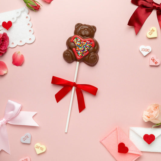 a chocolate bear lollipop with sprinkles and a red bow