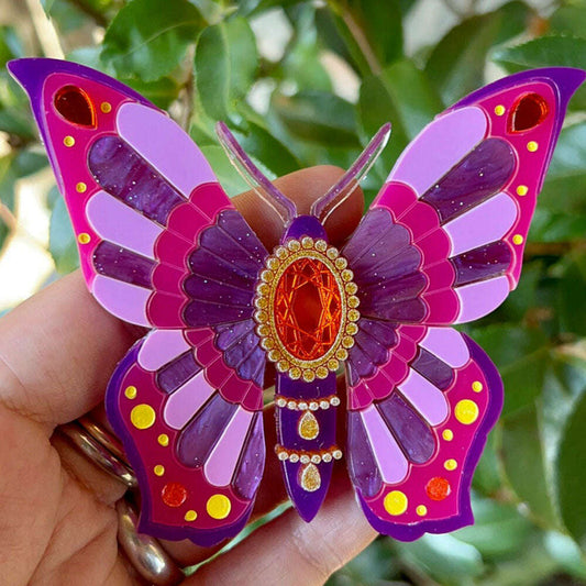 a hand holding a purple and pink butterfly brooch