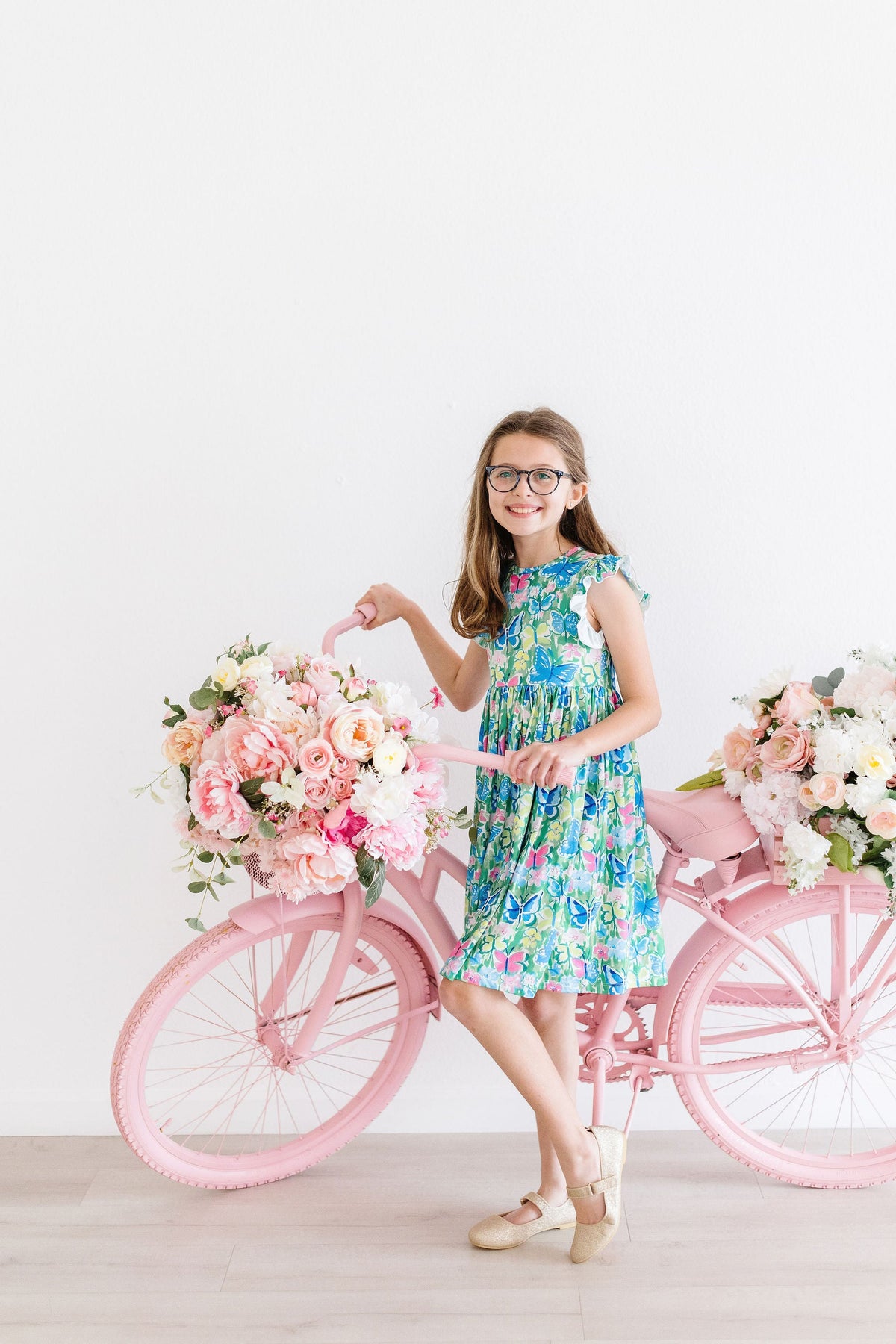 a girl in a dress with flowers on a pink bicycle