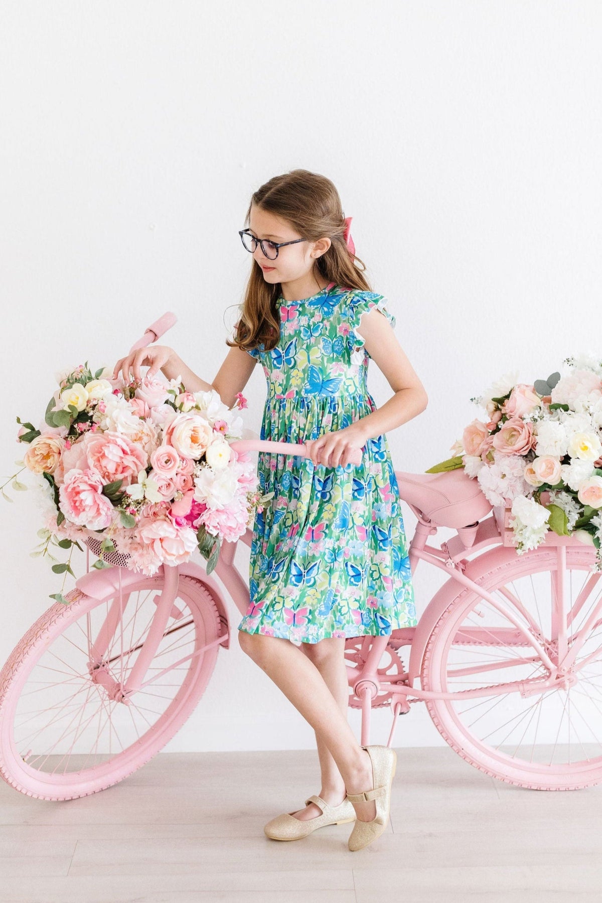 a girl in a dress and glasses with a bicycle full of flowers