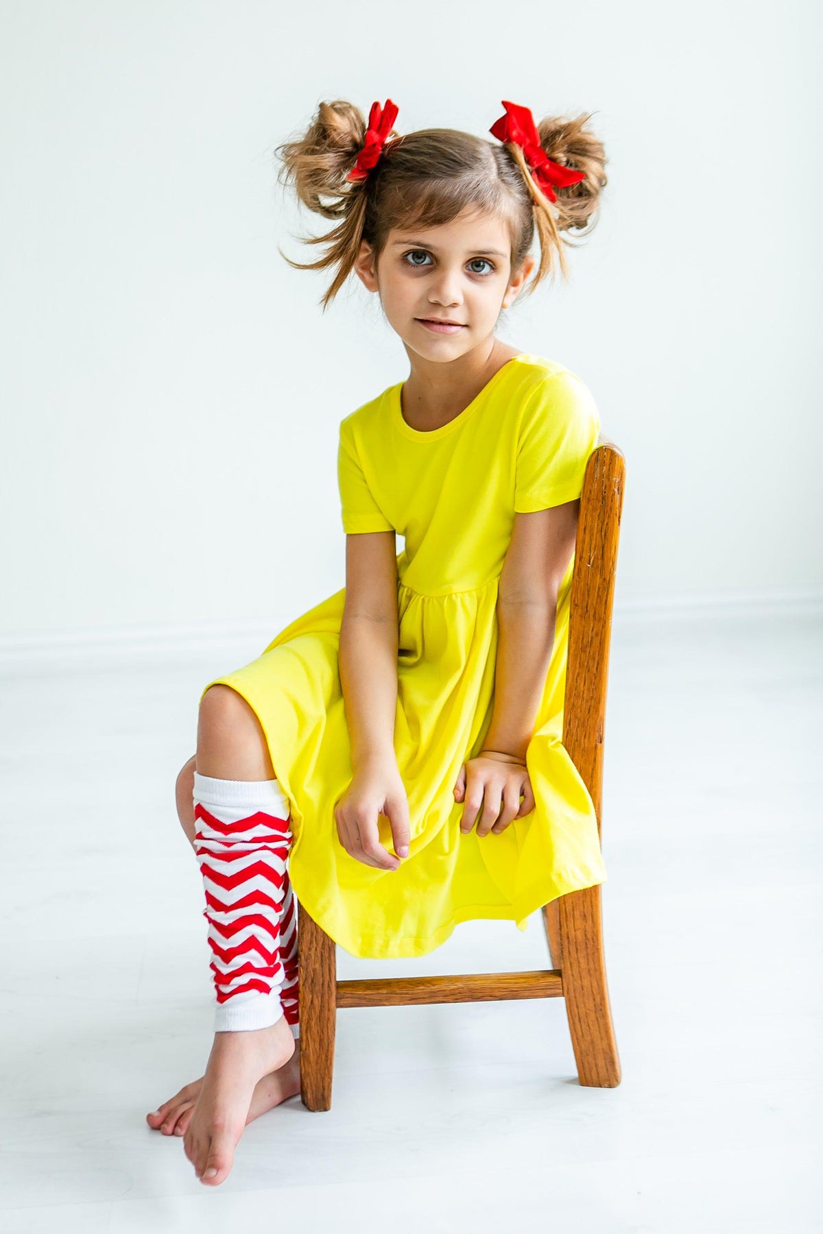 a girl in a yellow dress and red and white striped socks sitting on a chair