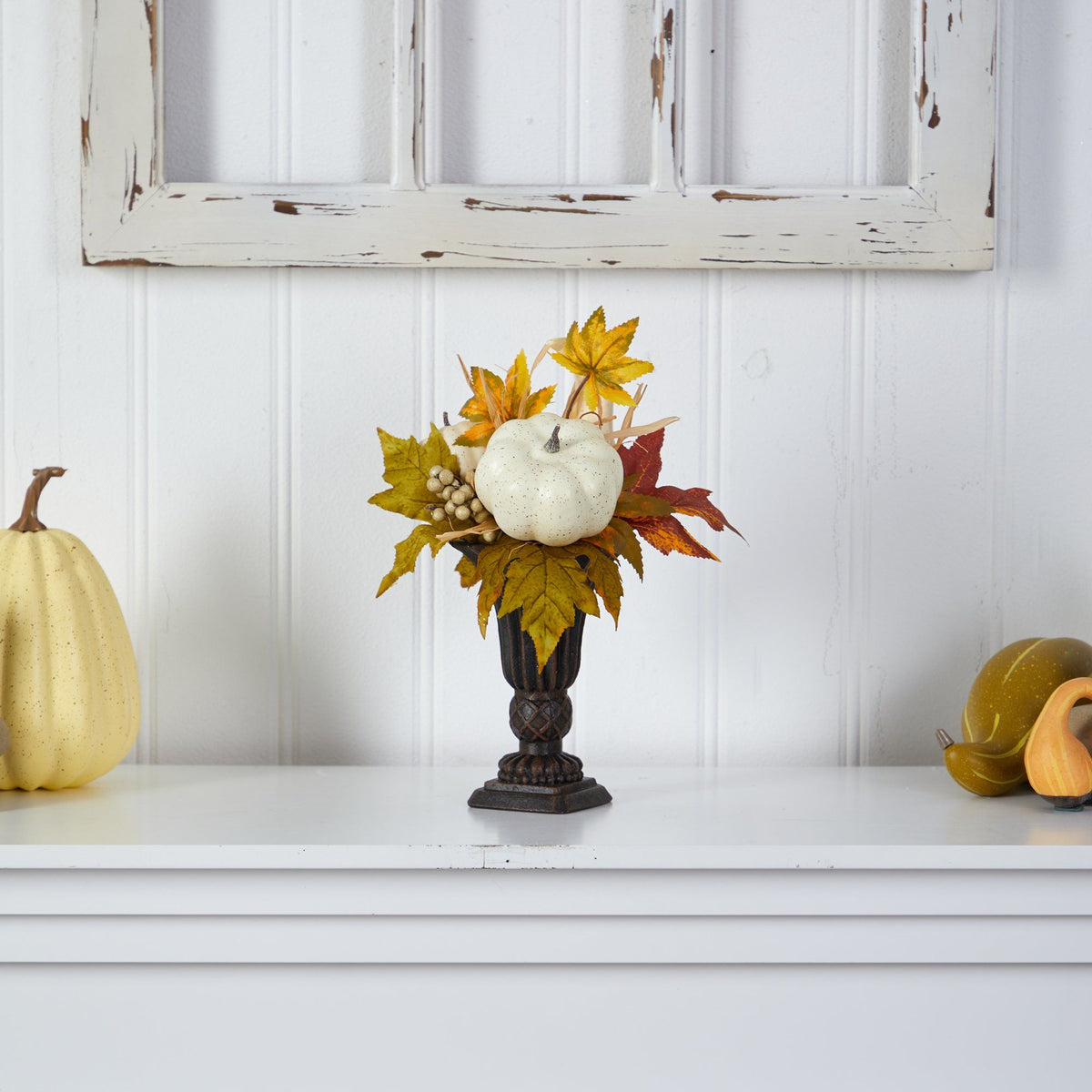 a vase with leaves and pumpkins on a white shelf