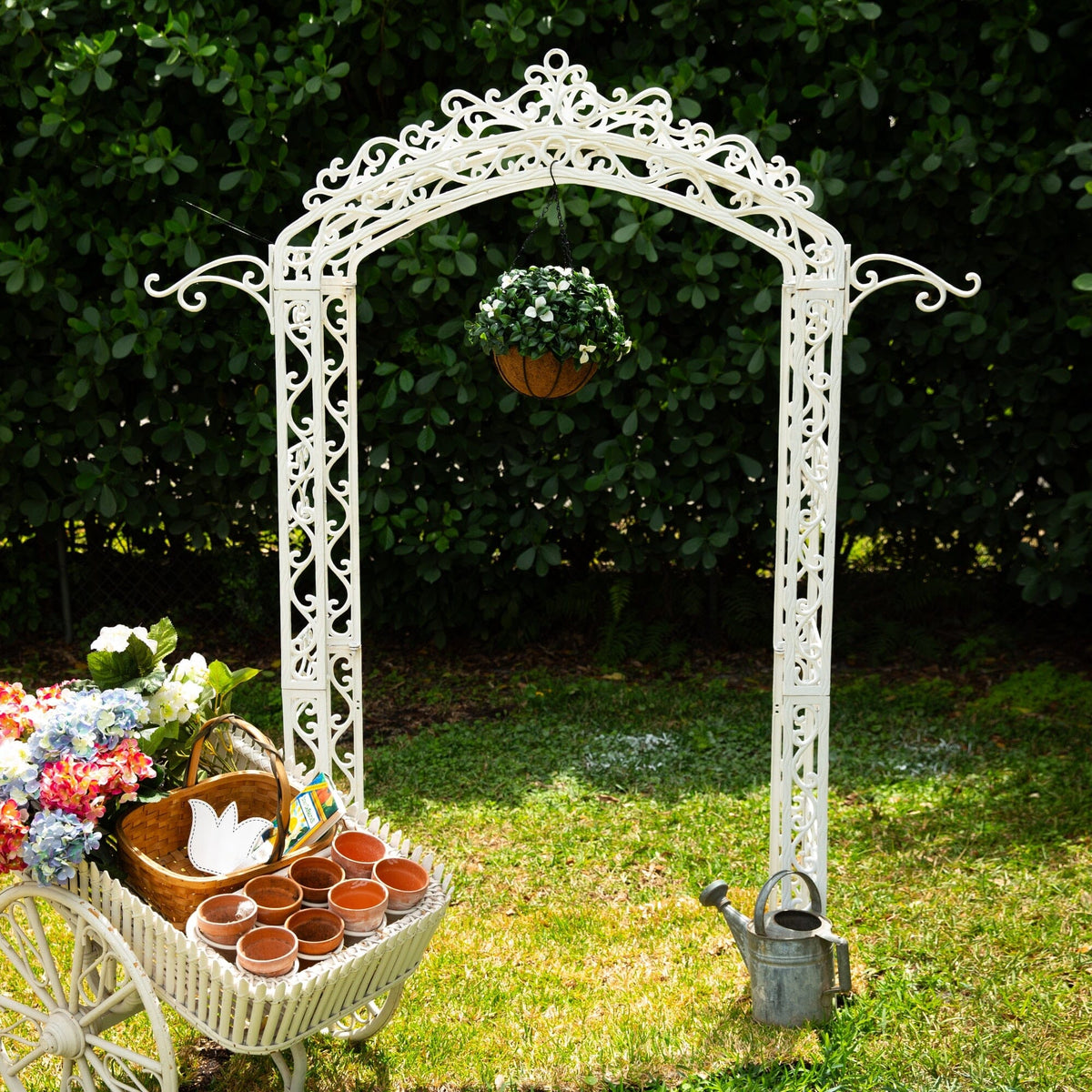 a white arch with a cart full of flowers and potted plants