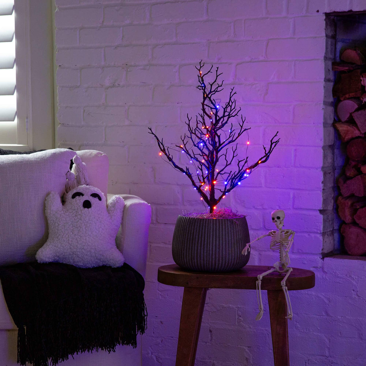 a tree with lights in a pot next to a white brick wall