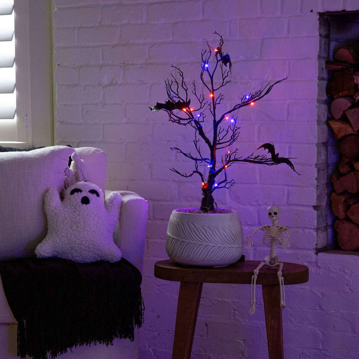 a tree with lights in a pot next to a white brick wall
