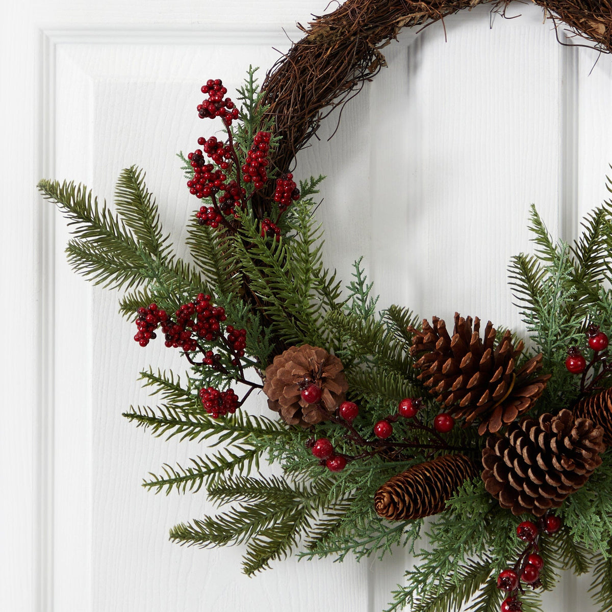 a wreath with pine cones and berries on a door