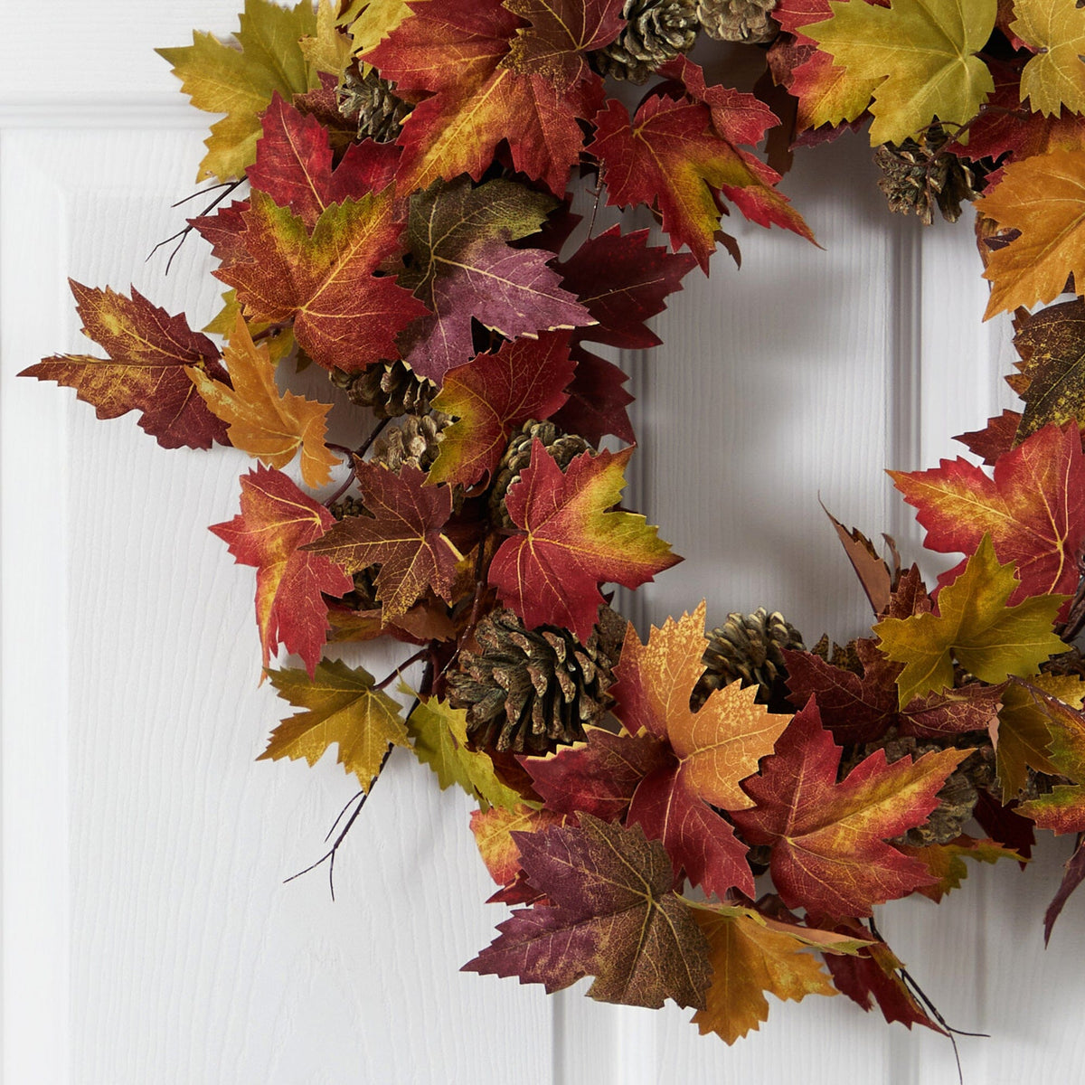 a wreath with leaves and pine cones on a white door