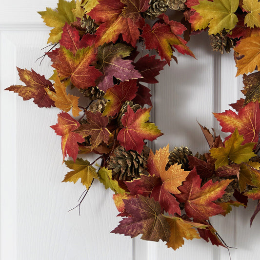 a wreath with leaves and pine cones on a white door