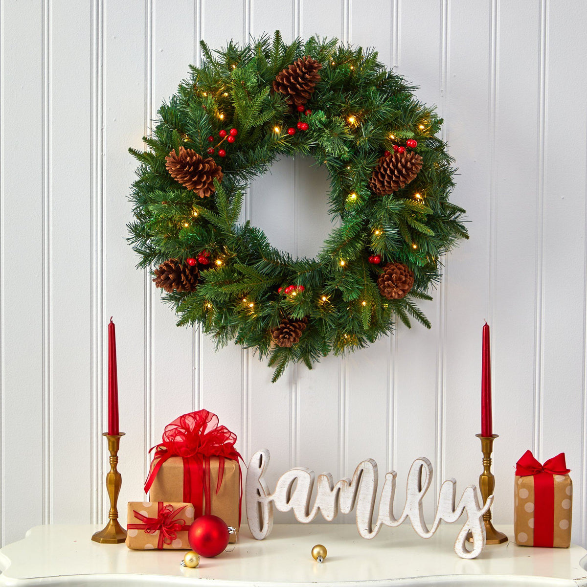 a wreath with lights and pine cones on a white table