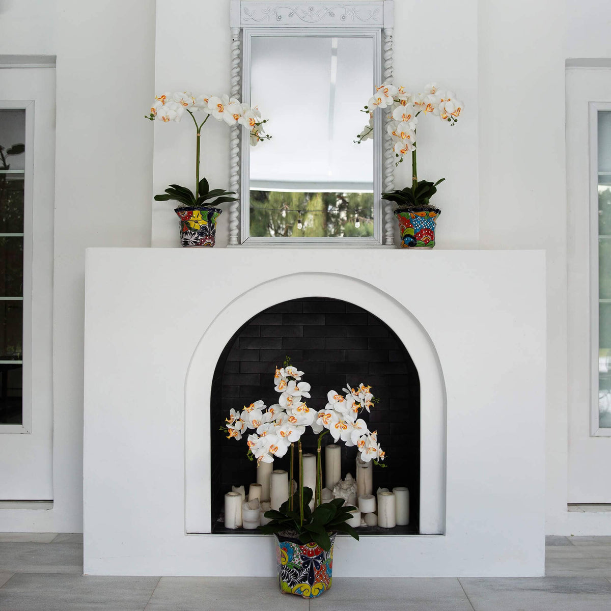 a white fireplace with white flowers and a mirror