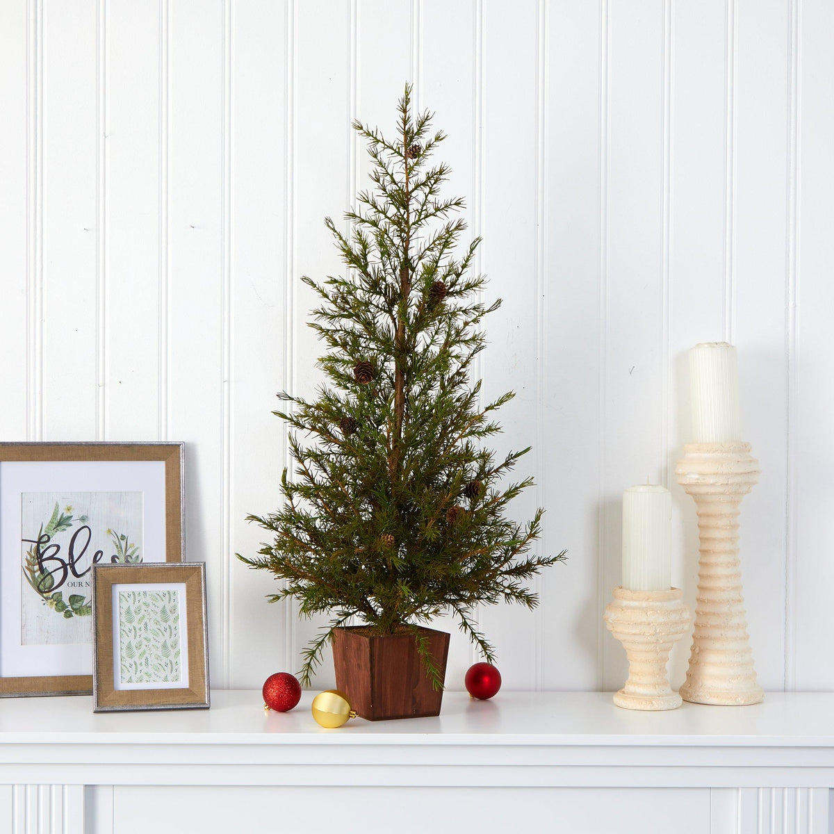 a small tree in a pot with candles and picture frames