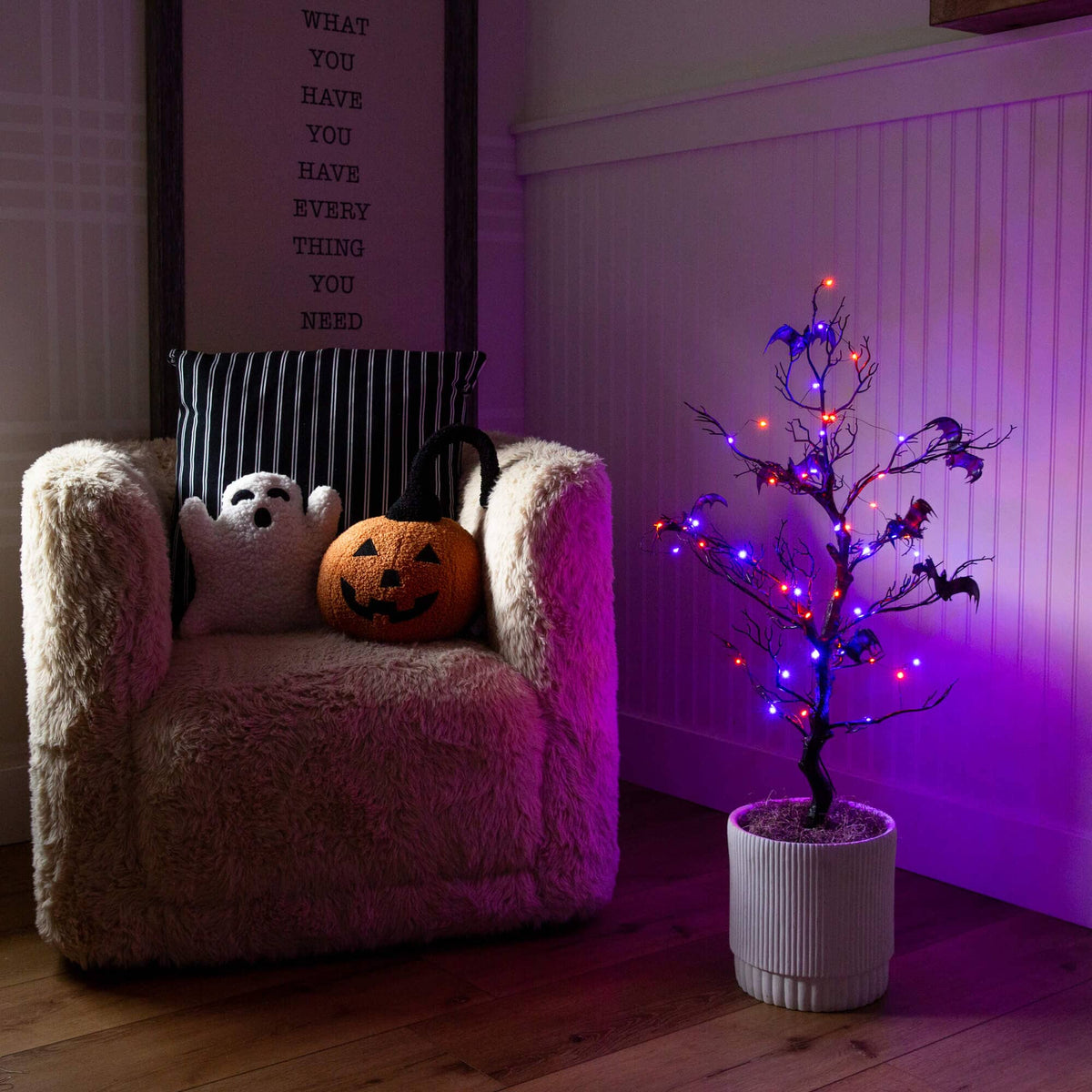 a chair with a pumpkin on it and a lit tree in a pot