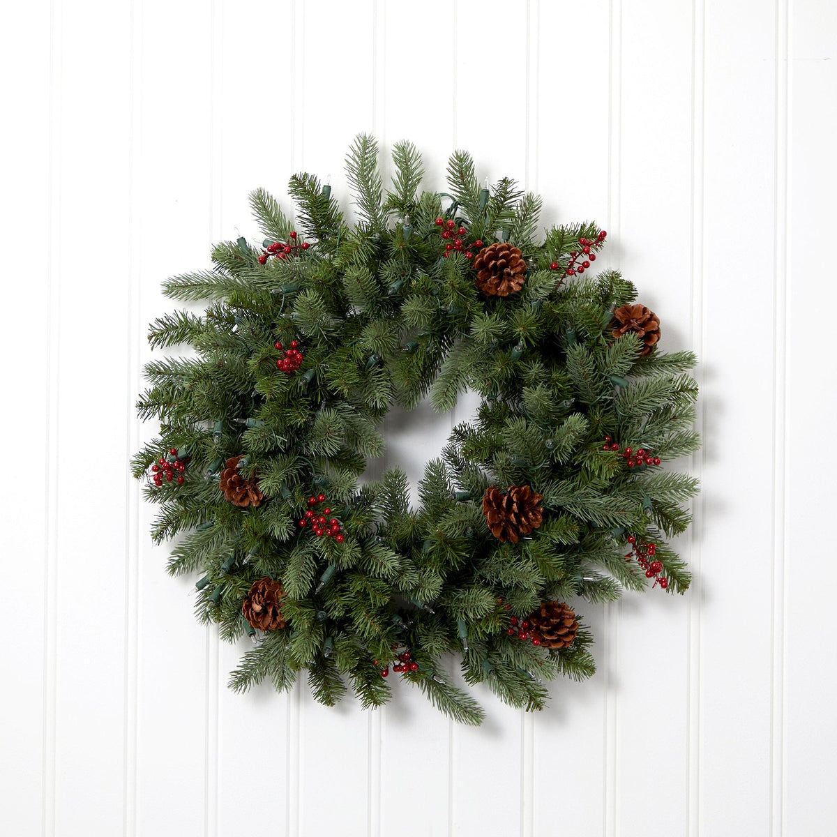 a wreath with pine cones and berries on a white wall