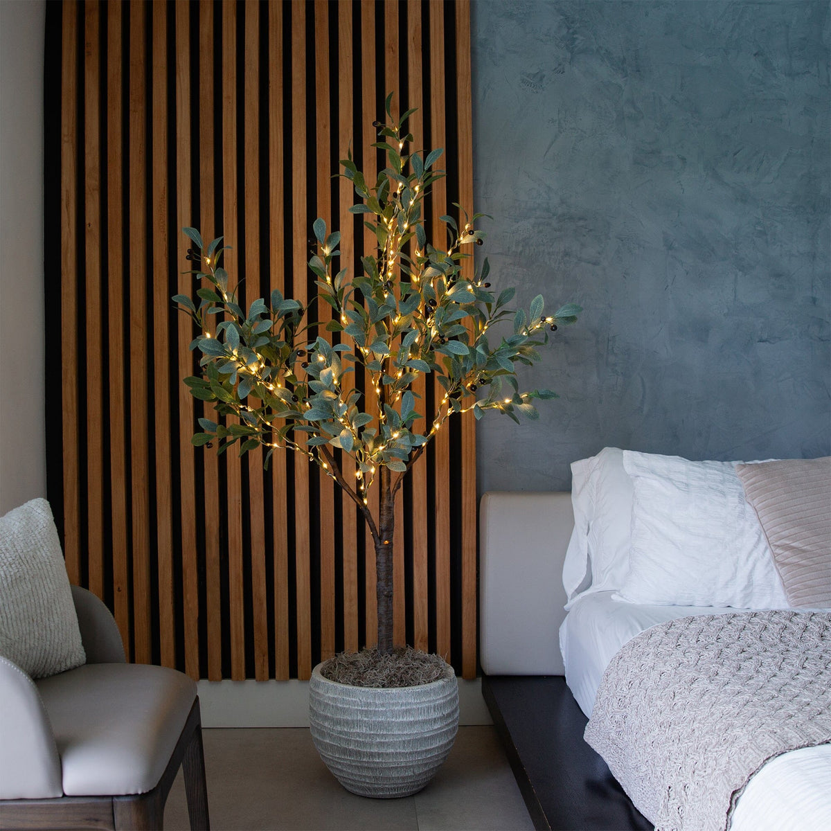a tree in a pot with lights in front of a bed