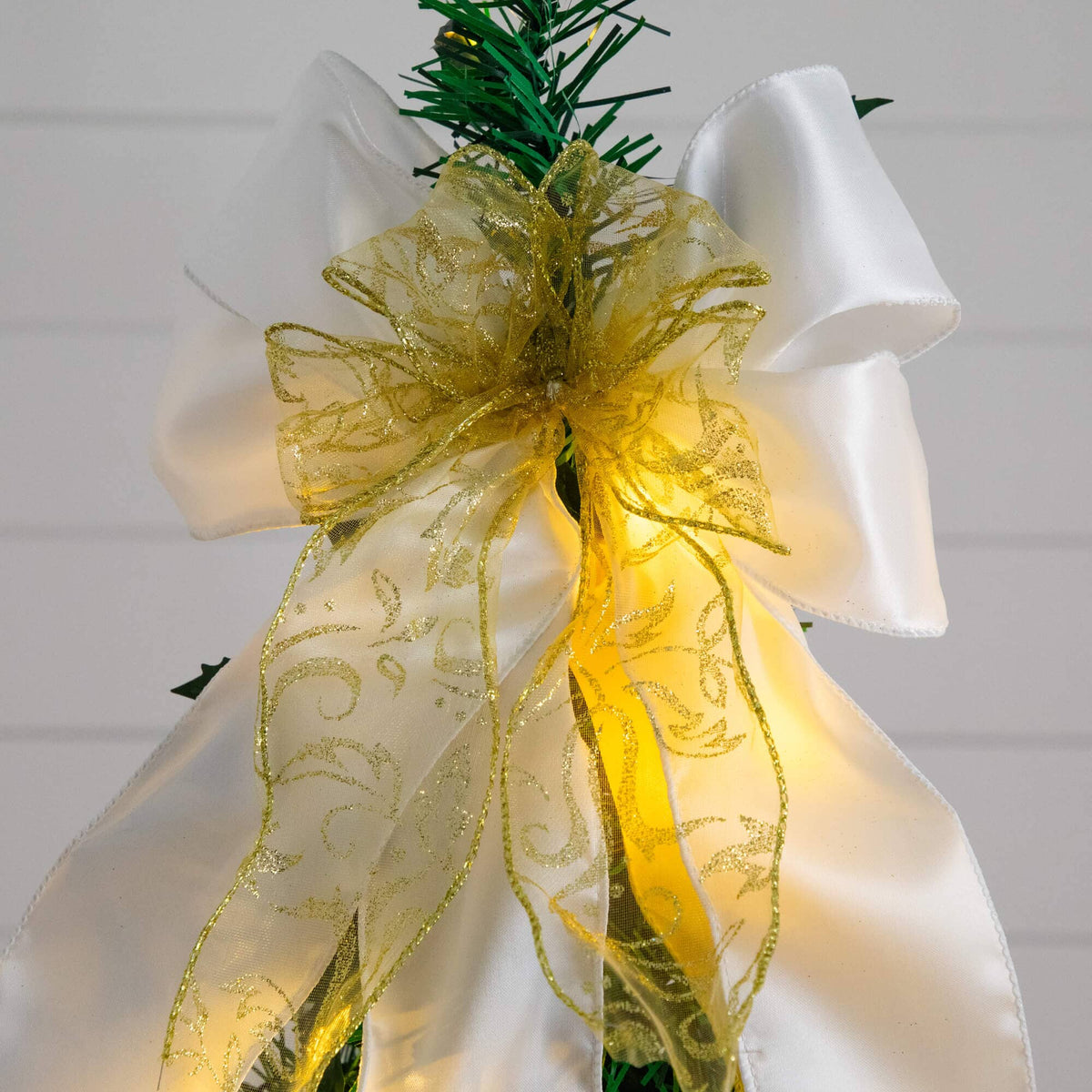 a white bow with gold ribbon on top of a green christmas tree