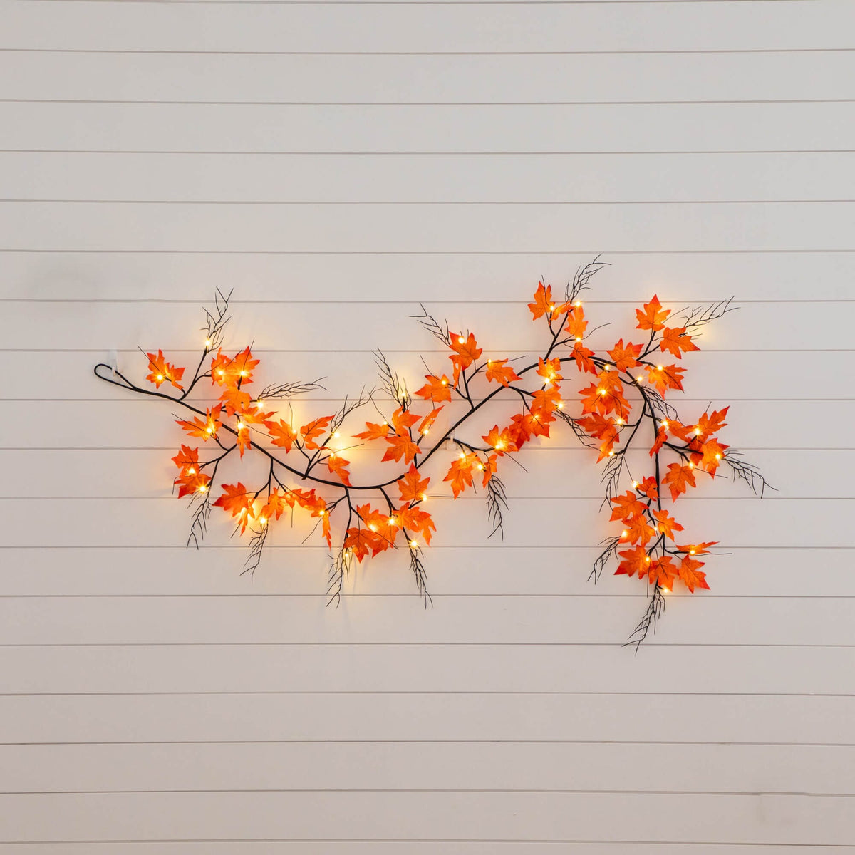 a branch with orange leaves and lights on a white wall