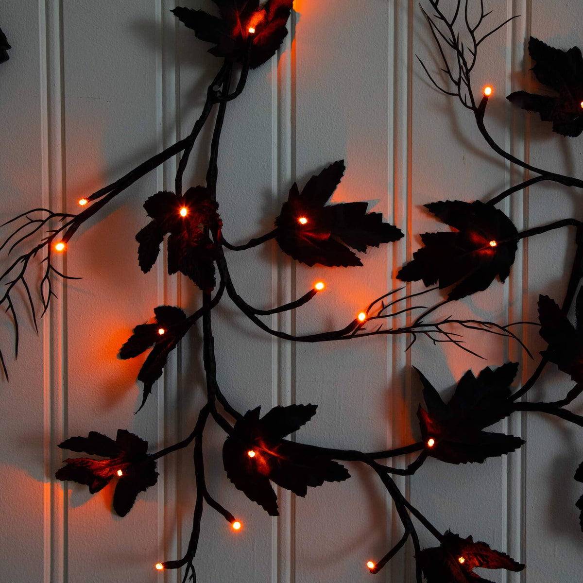 a black leaves with orange lights on a white wall