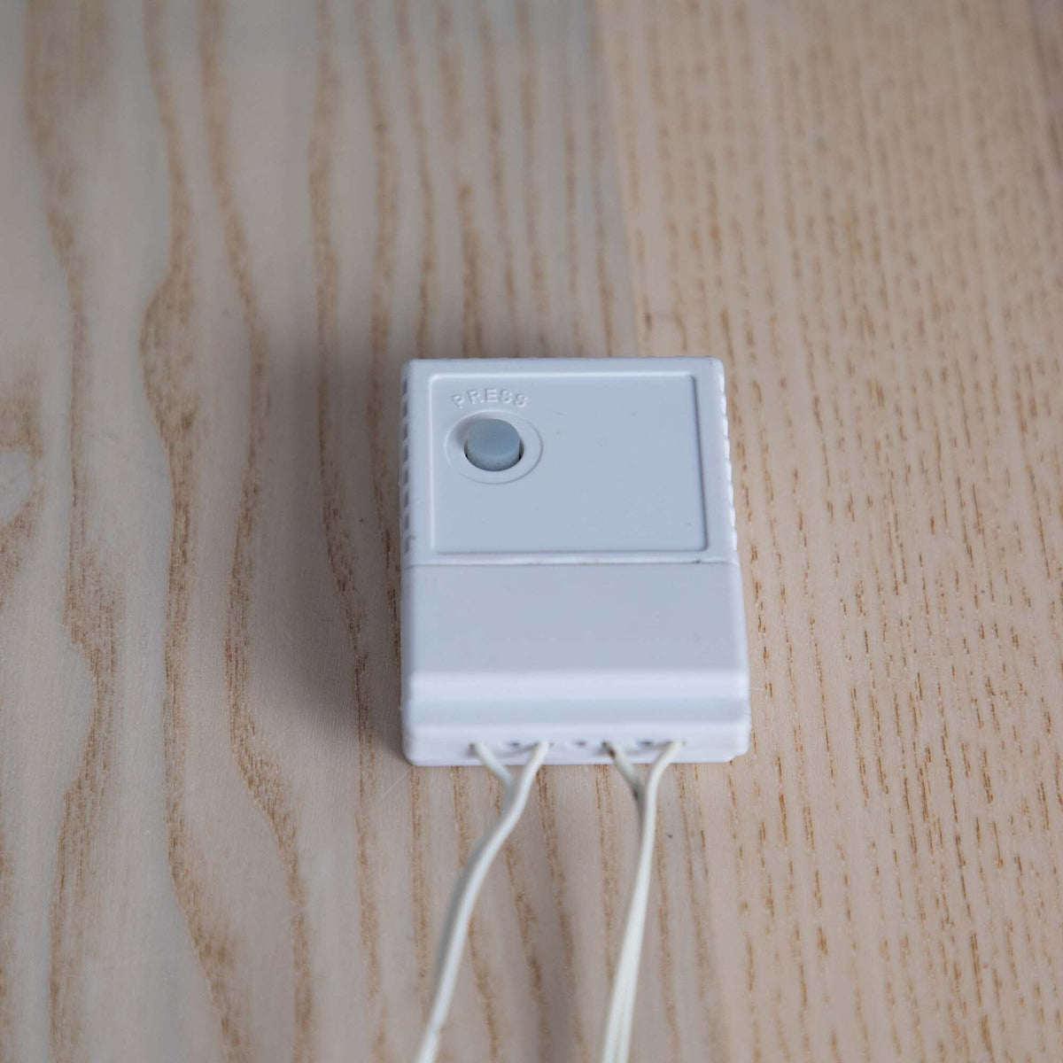 a white rectangular object with a button and wires on a wood surface