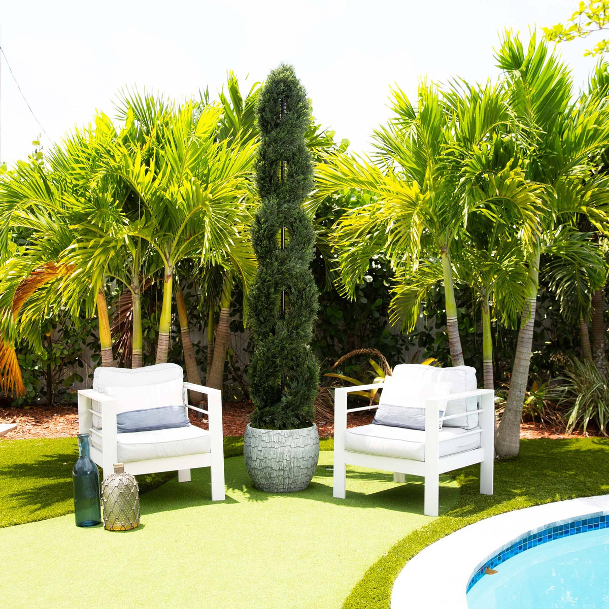 a pool with white chairs and a tall tree in front of it