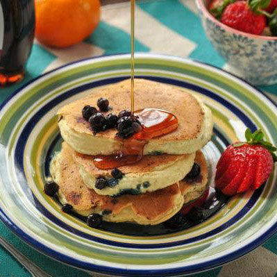 Stack of pancakes with blueberries and syrup on a colorful plate with strawberries.