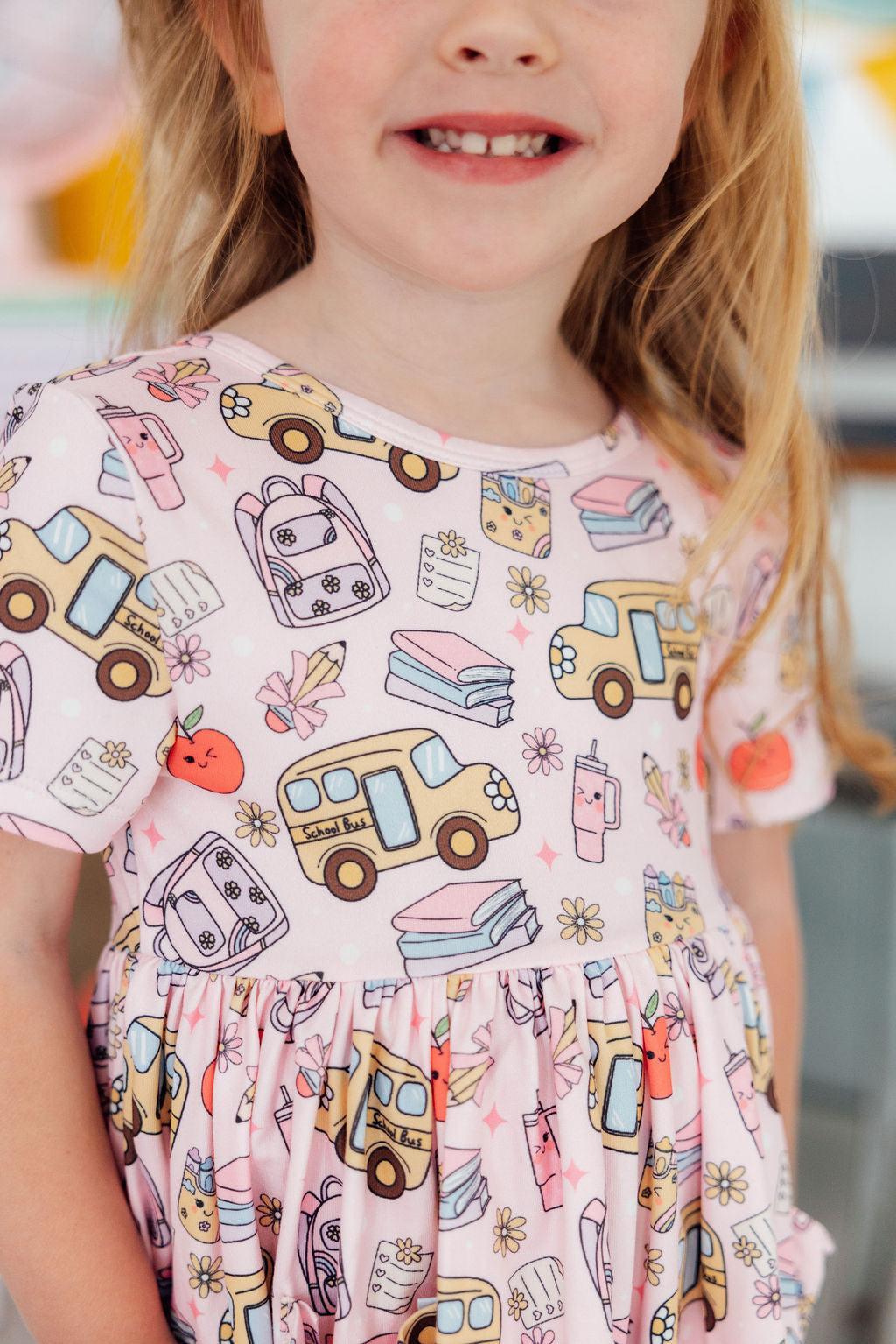 a girl wearing a pink dress with school themed designs
